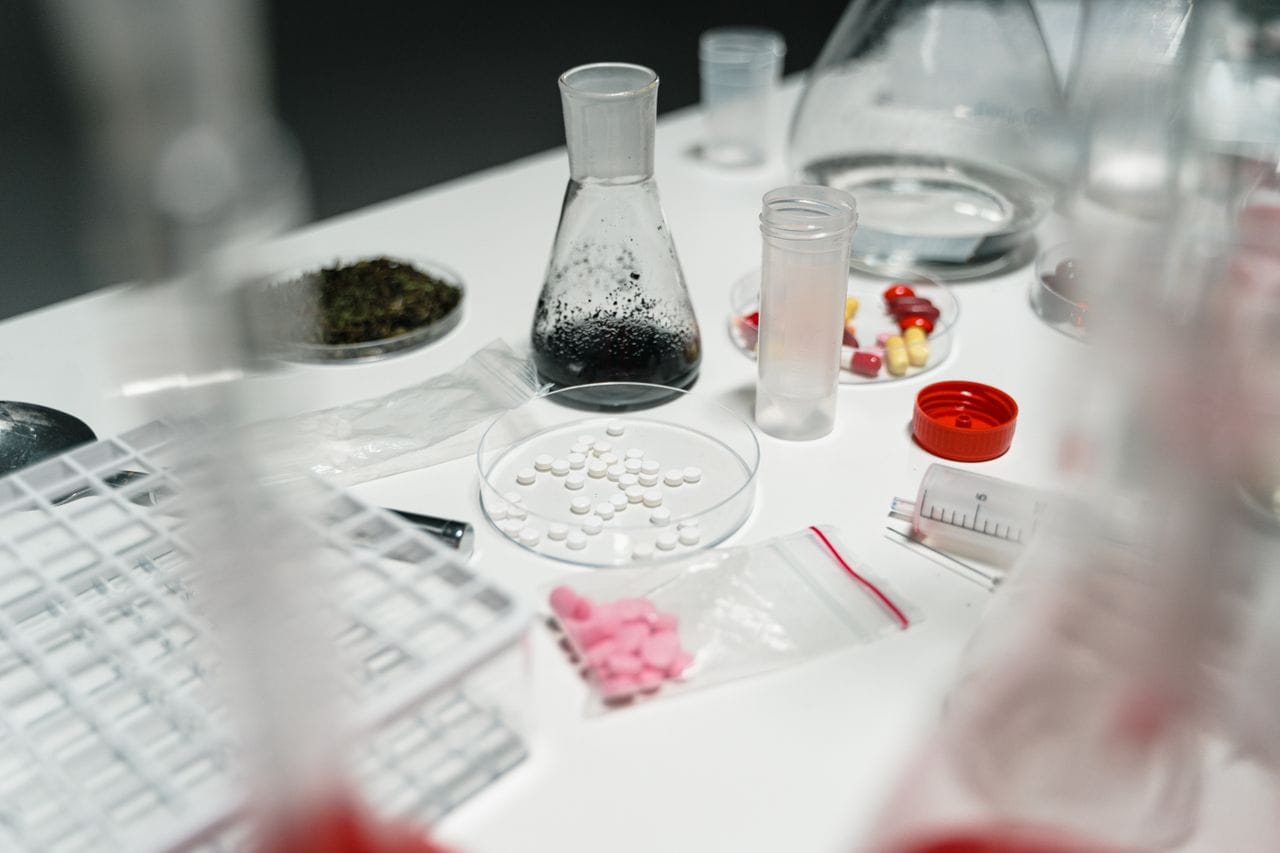 A laboratory table displaying pills, petri dishes, and chemical beakers for scientific research.